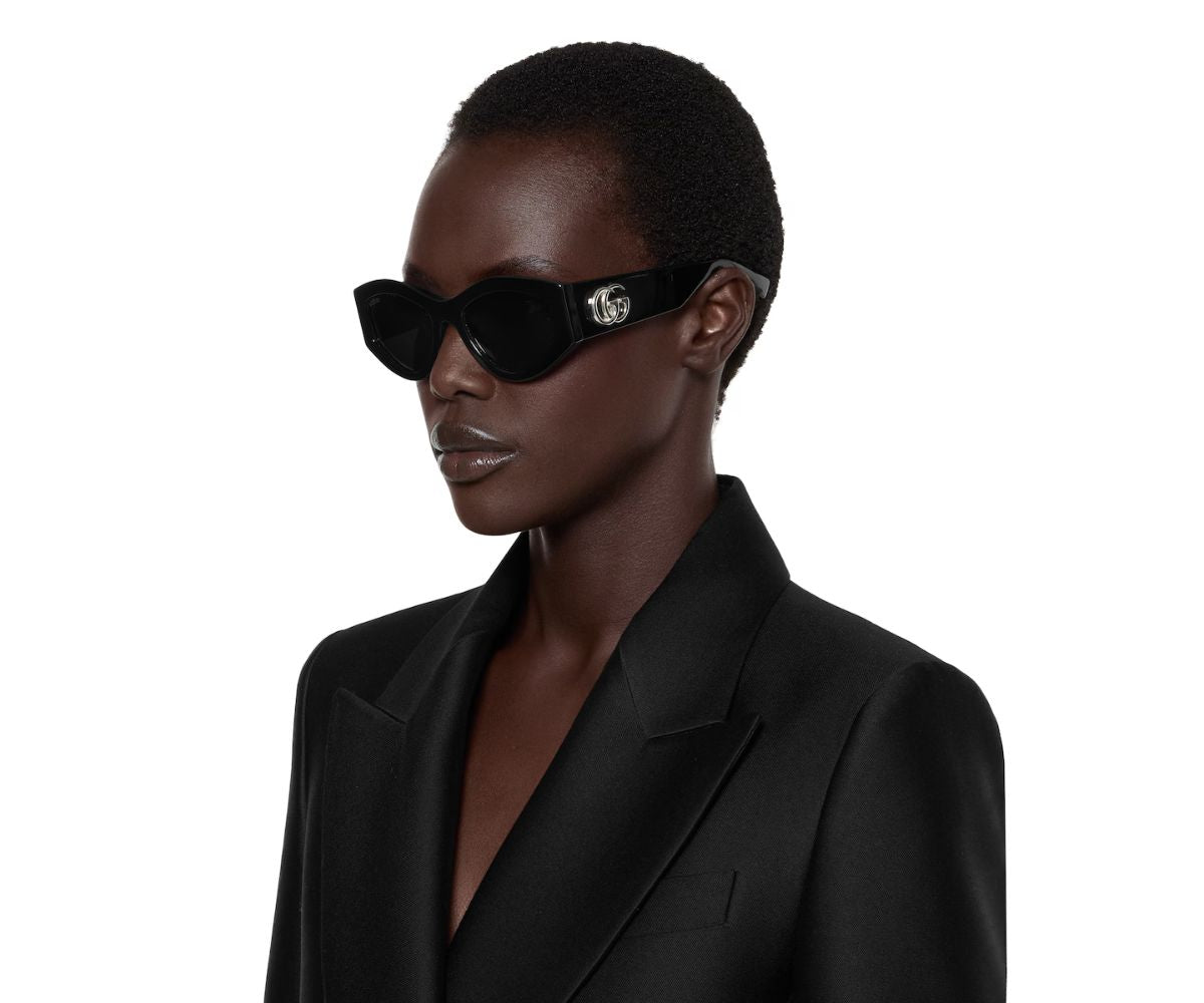 Black cat-eye sunglasses with silver logo, worn by model in black blazer, luxury designer style